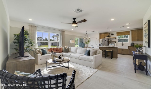 living room with ceiling fan with notable chandelier, light wood-type flooring, and sink