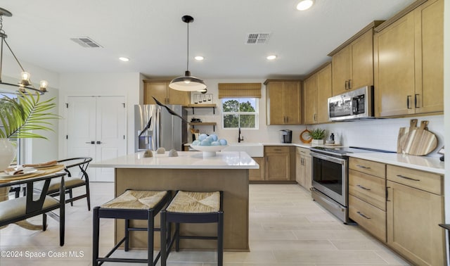 kitchen featuring decorative light fixtures, a kitchen island, sink, and stainless steel appliances