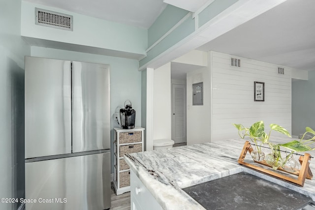 kitchen featuring hardwood / wood-style flooring, stainless steel fridge, light stone counters, and wooden walls