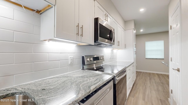 kitchen with light stone countertops, white cabinetry, tasteful backsplash, appliances with stainless steel finishes, and light wood-type flooring