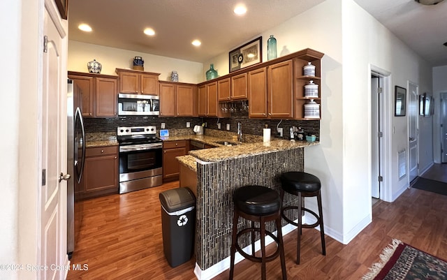 kitchen with a kitchen breakfast bar, tasteful backsplash, dark hardwood / wood-style flooring, kitchen peninsula, and stainless steel appliances