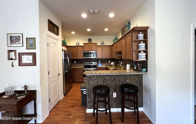 kitchen with kitchen peninsula, appliances with stainless steel finishes, decorative backsplash, a breakfast bar, and dark wood-type flooring