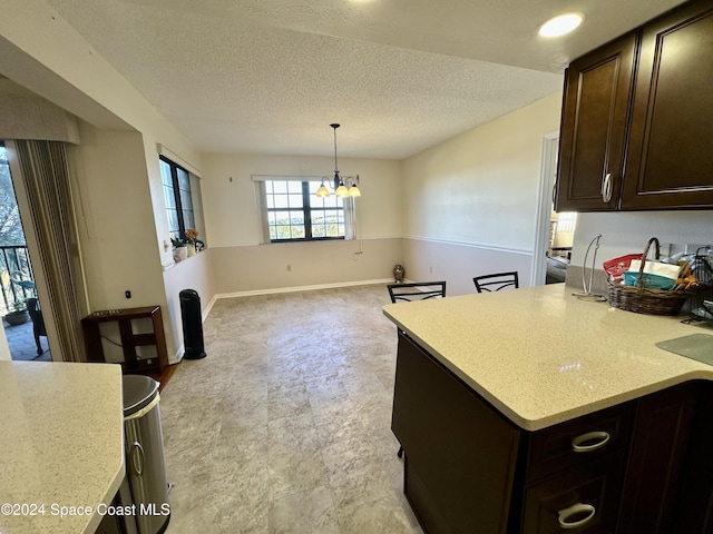 kitchen featuring dark brown cabinets, a textured ceiling, hanging light fixtures, and a notable chandelier