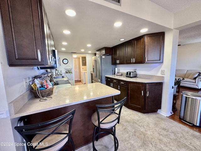 kitchen featuring light stone counters, kitchen peninsula, a breakfast bar, dark brown cabinets, and appliances with stainless steel finishes