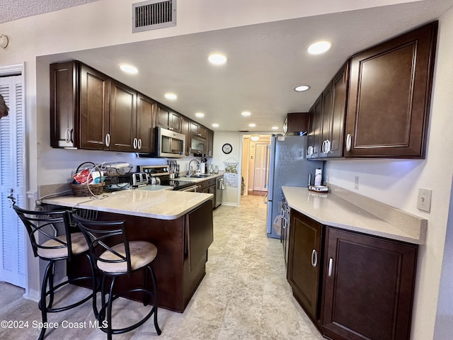 kitchen with kitchen peninsula, appliances with stainless steel finishes, a kitchen bar, dark brown cabinets, and sink