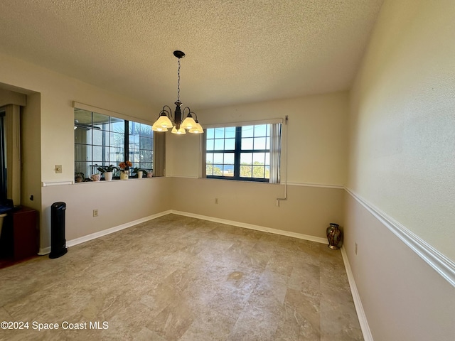 unfurnished dining area with a textured ceiling and a notable chandelier