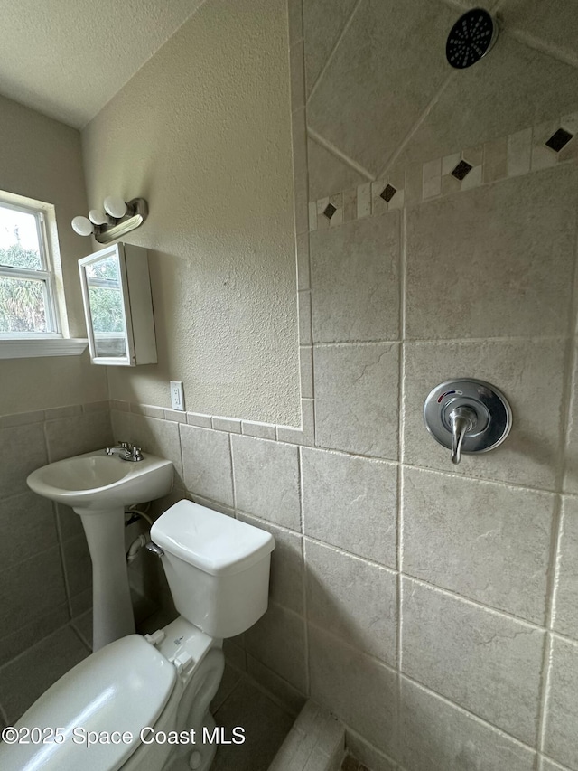 bathroom featuring tile walls, toilet, a tile shower, and a textured ceiling