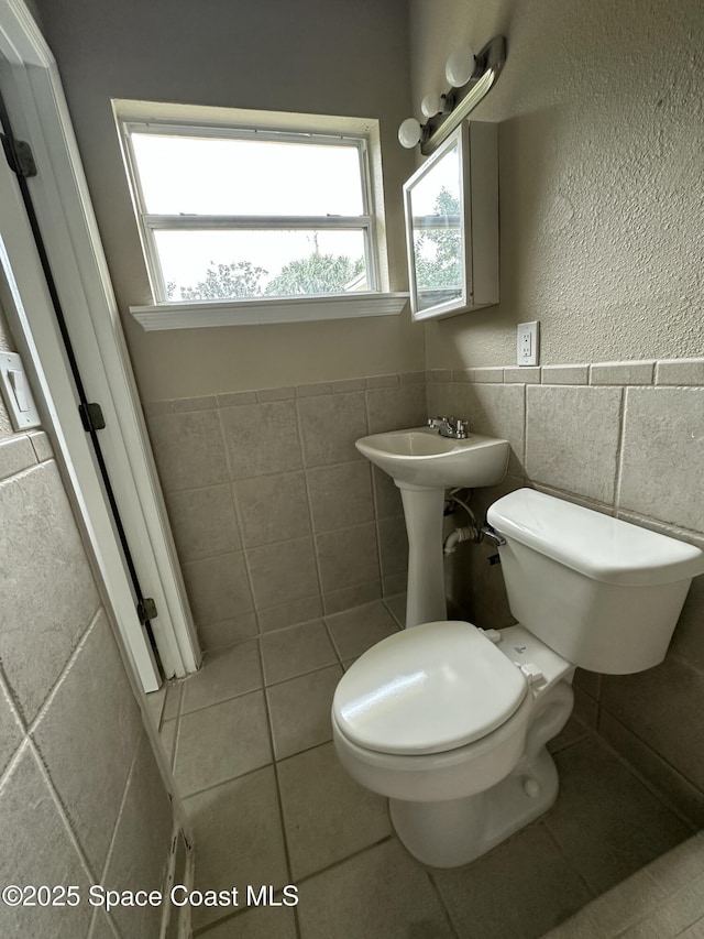 bathroom with toilet, tile patterned flooring, and tile walls