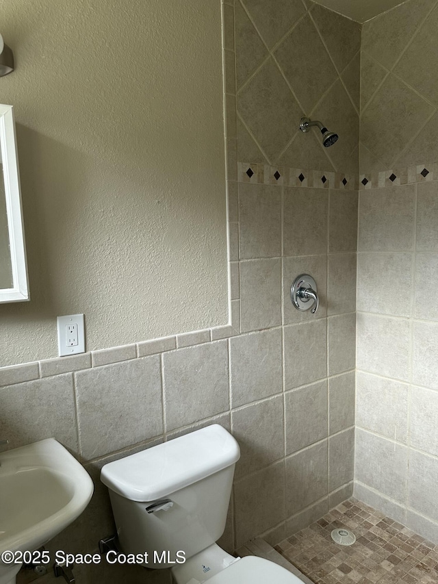 bathroom featuring toilet, a tile shower, tile walls, and sink