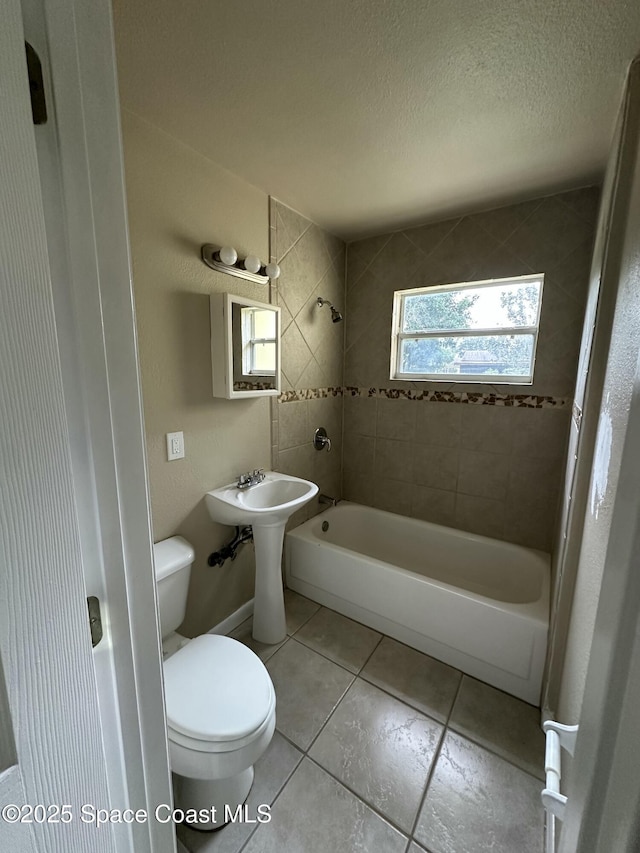 full bathroom featuring toilet, tiled shower / bath, tile patterned floors, sink, and a textured ceiling