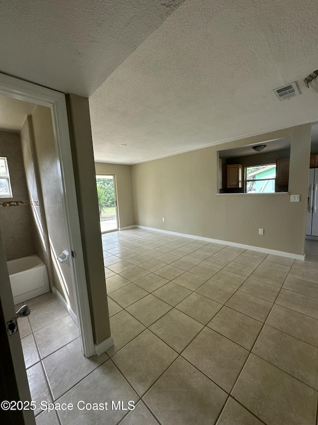 spare room featuring a textured ceiling, light tile patterned floors, and a healthy amount of sunlight