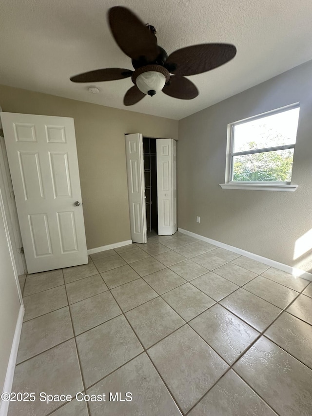 unfurnished bedroom with ceiling fan, light tile patterned floors, a closet, and a textured ceiling