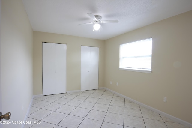 unfurnished bedroom featuring ceiling fan, light tile patterned floors, a textured ceiling, and two closets