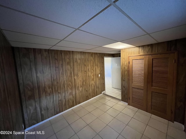 basement featuring a drop ceiling and wooden walls