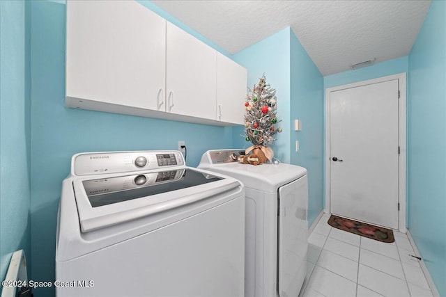 laundry room featuring washer and dryer, light tile patterned flooring, cabinets, and a textured ceiling