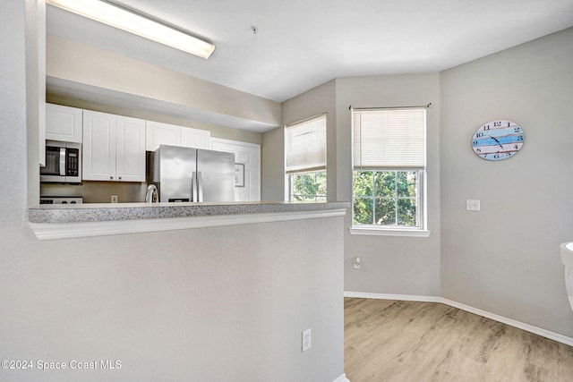 kitchen featuring kitchen peninsula, white cabinets, light wood-type flooring, and appliances with stainless steel finishes