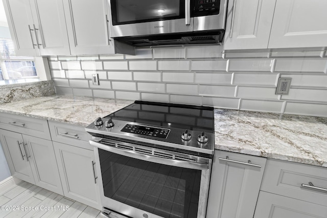 kitchen featuring white cabinets, decorative backsplash, light stone countertops, and appliances with stainless steel finishes