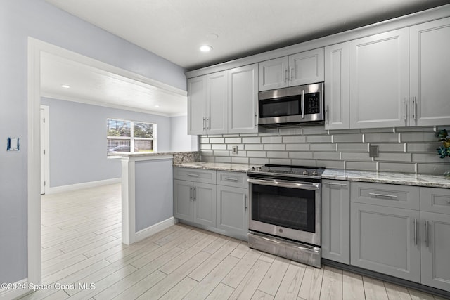 kitchen with appliances with stainless steel finishes, backsplash, crown molding, light hardwood / wood-style flooring, and gray cabinets