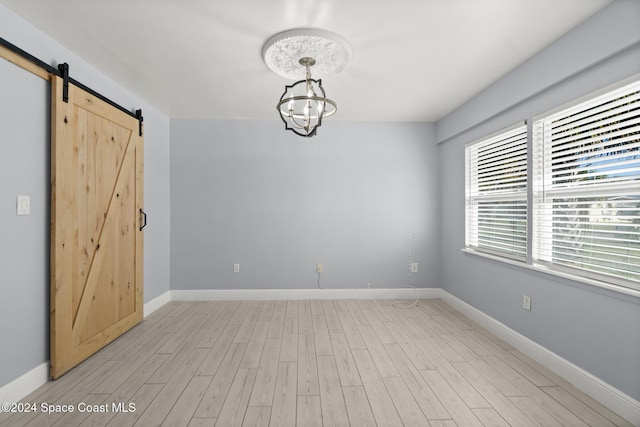 spare room featuring a barn door, light hardwood / wood-style flooring, and an inviting chandelier