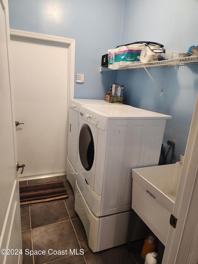 washroom featuring washing machine and dryer, dark tile patterned floors, and sink