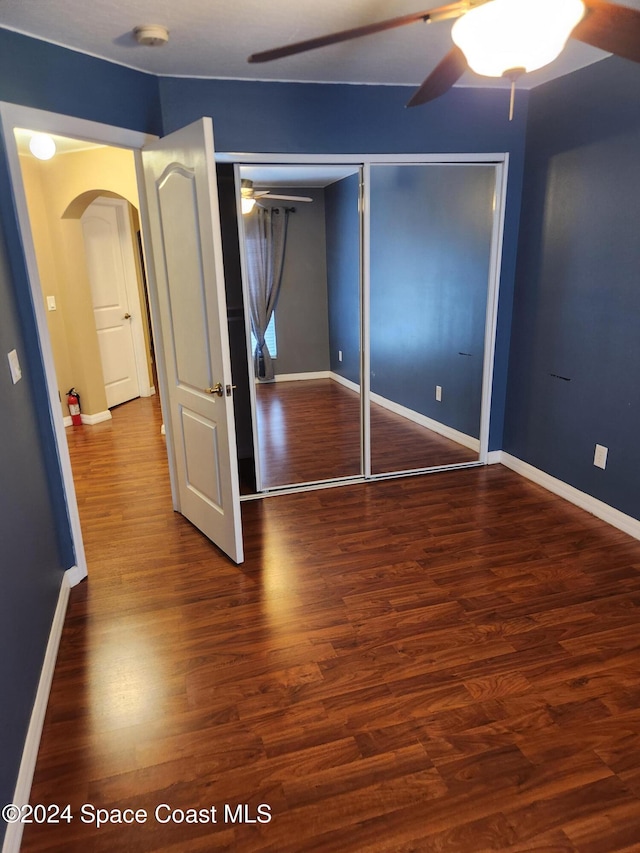 unfurnished bedroom with a closet, dark wood-type flooring, and ceiling fan