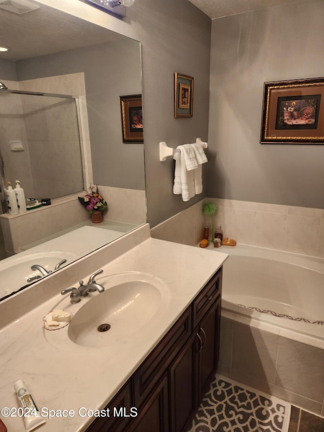 bathroom with tile patterned flooring, a textured ceiling, vanity, and tiled tub