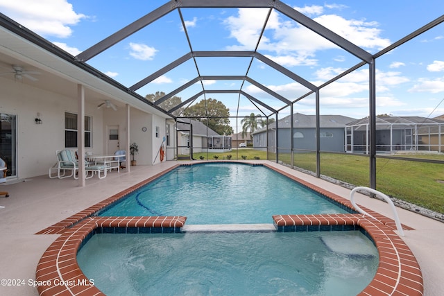 view of pool featuring a lawn, glass enclosure, ceiling fan, and a patio