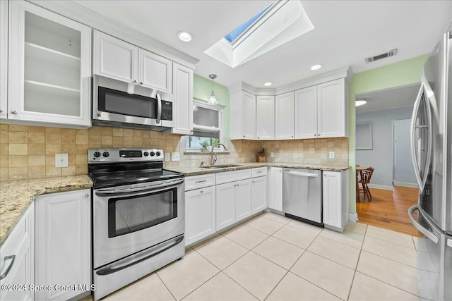 kitchen with appliances with stainless steel finishes, a skylight, sink, pendant lighting, and white cabinetry