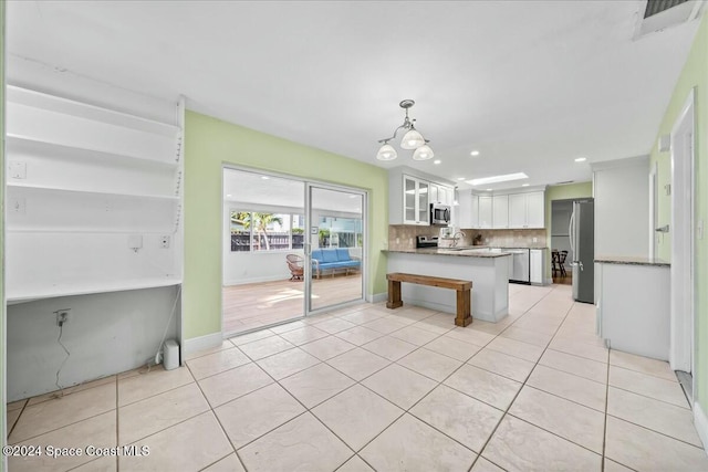 kitchen featuring kitchen peninsula, appliances with stainless steel finishes, decorative backsplash, light tile patterned floors, and white cabinetry