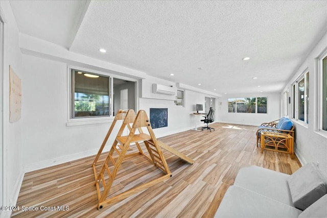 living room featuring wood-type flooring, a textured ceiling, and a wall unit AC