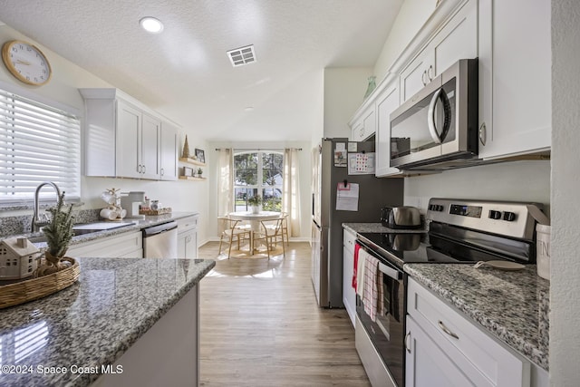 kitchen featuring light stone countertops, appliances with stainless steel finishes, vaulted ceiling, sink, and white cabinetry