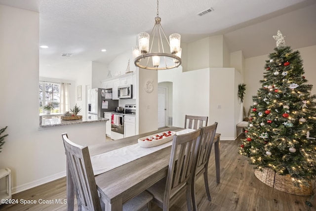 dining area with a textured ceiling, lofted ceiling, dark wood-type flooring, and an inviting chandelier