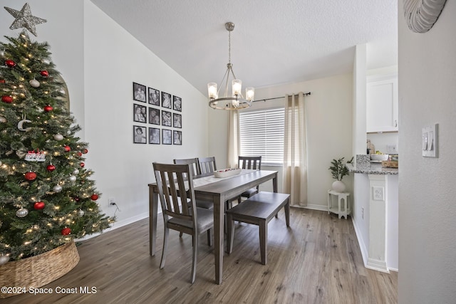 dining space with a textured ceiling, light wood-type flooring, vaulted ceiling, and a notable chandelier