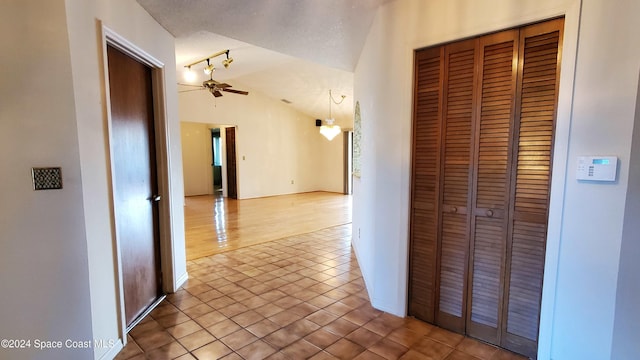 hall featuring light tile patterned floors, a textured ceiling, and lofted ceiling