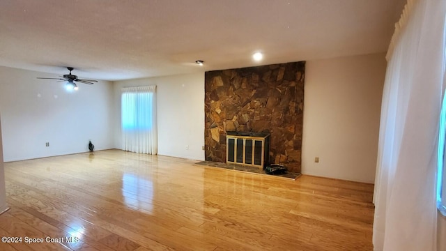 unfurnished living room featuring wood-type flooring, a stone fireplace, and ceiling fan