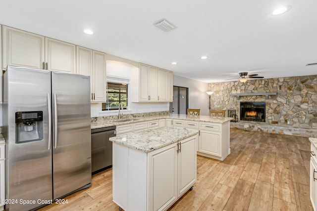 kitchen with appliances with stainless steel finishes, sink, a center island, light hardwood / wood-style floors, and a stone fireplace