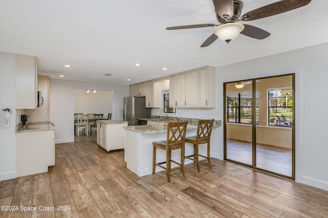 kitchen featuring ceiling fan, stainless steel appliances, kitchen peninsula, light hardwood / wood-style floors, and a kitchen island