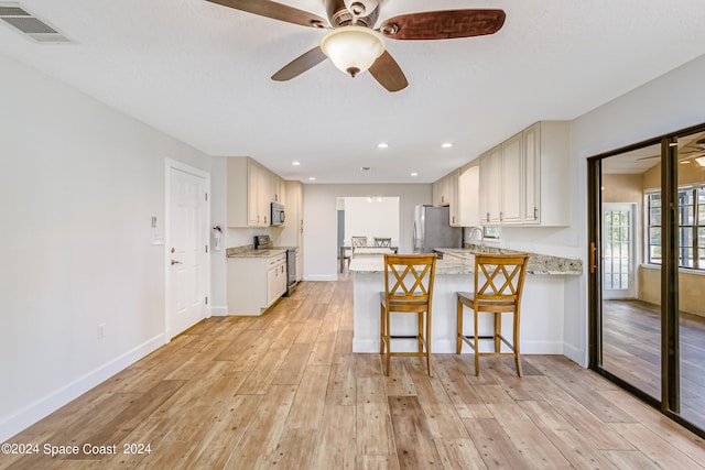 kitchen featuring kitchen peninsula, appliances with stainless steel finishes, light wood-type flooring, light stone countertops, and a kitchen bar