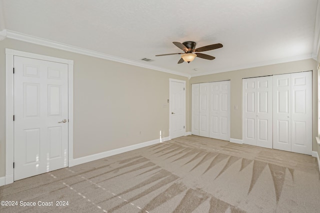 unfurnished bedroom featuring carpet flooring, ceiling fan, crown molding, and two closets