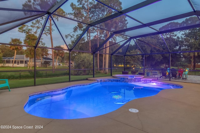 pool at dusk featuring a lanai, a patio area, and an in ground hot tub