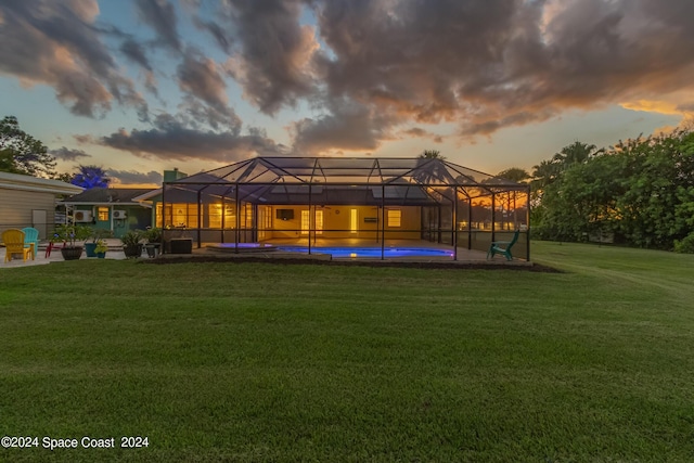 back house at dusk with a patio area, a lanai, and a lawn