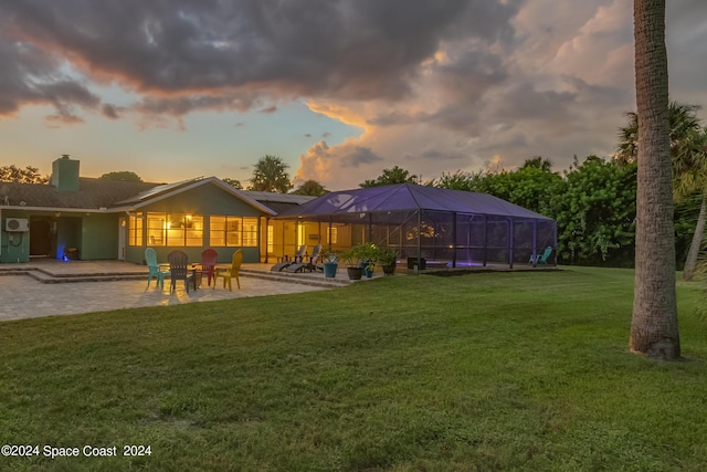 back house at dusk featuring a lawn, a patio area, and a lanai