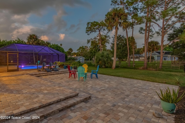 playground at dusk with a lanai, a lawn, a patio, and a pool