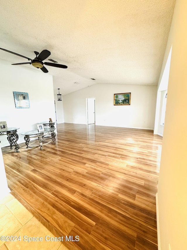 unfurnished living room featuring ceiling fan, lofted ceiling, a textured ceiling, and light hardwood / wood-style flooring