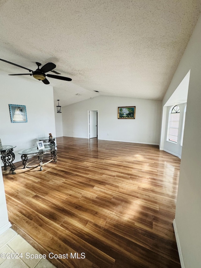 unfurnished living room featuring vaulted ceiling, wood-type flooring, ceiling fan, and a textured ceiling