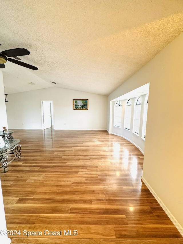 unfurnished living room featuring vaulted ceiling, wood-type flooring, ceiling fan, and a textured ceiling