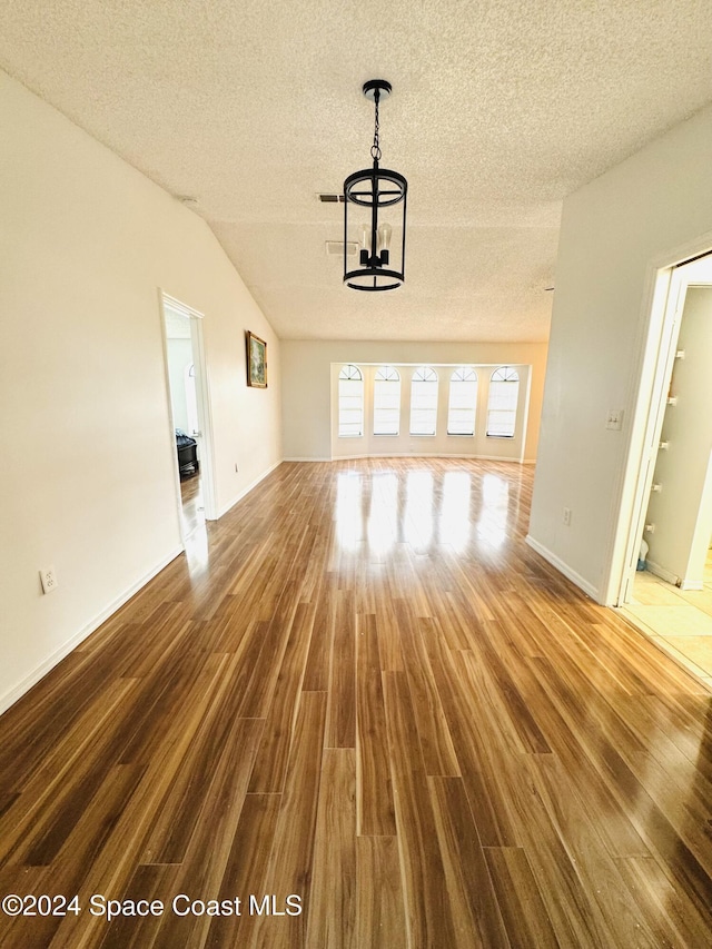 unfurnished living room with lofted ceiling, hardwood / wood-style floors, a textured ceiling, and an inviting chandelier