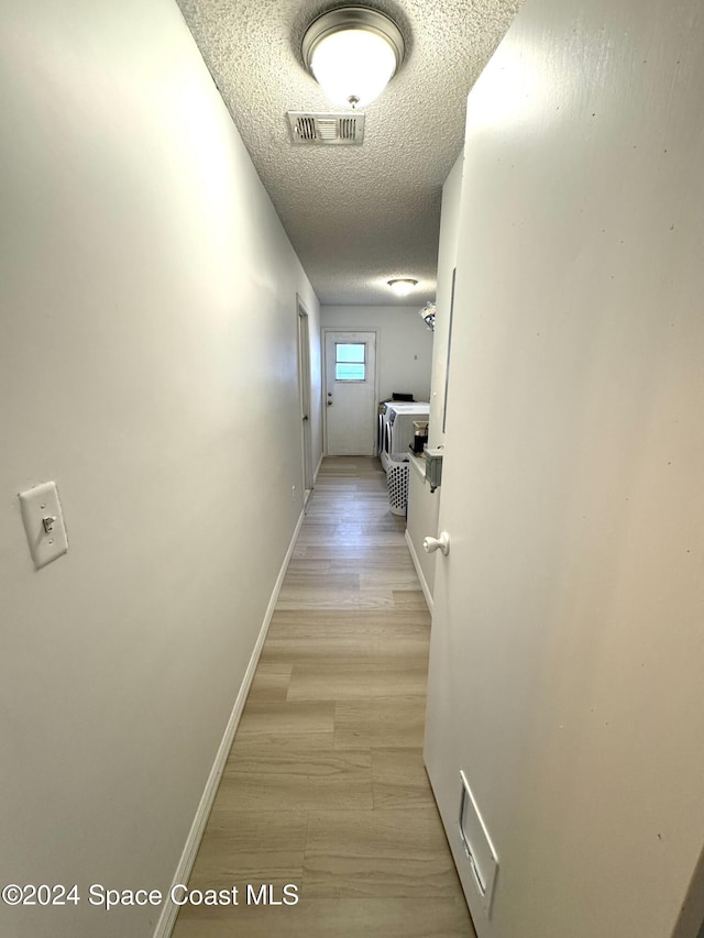 hallway with a textured ceiling and light hardwood / wood-style flooring