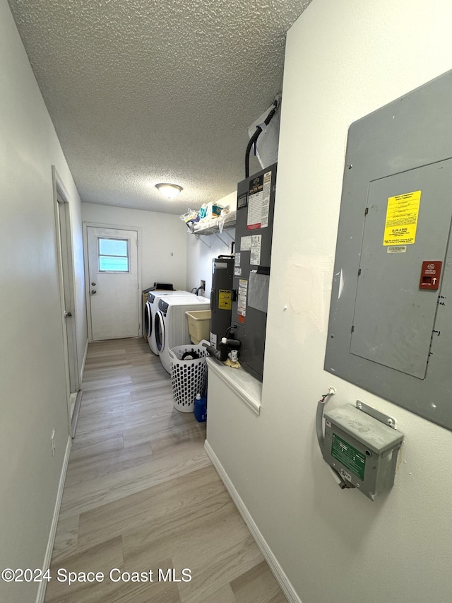 laundry area with heating unit, washer and clothes dryer, electric panel, a textured ceiling, and light hardwood / wood-style flooring