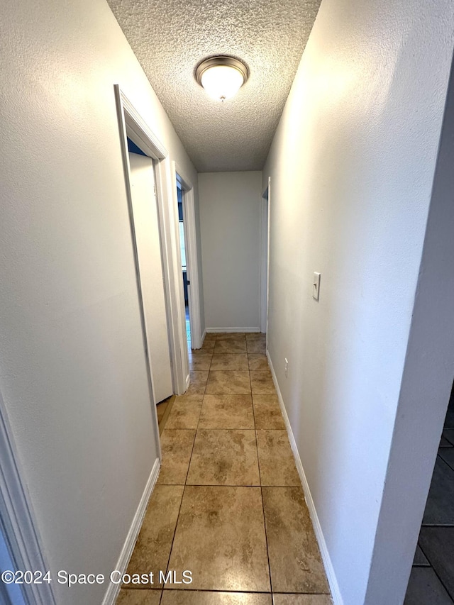 hall with tile patterned floors and a textured ceiling